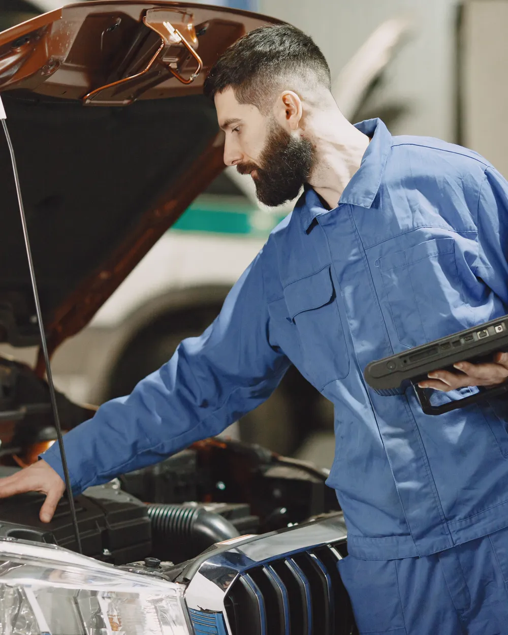 Mechanic inspecting a vehicle engine bay with a diagnostic tool