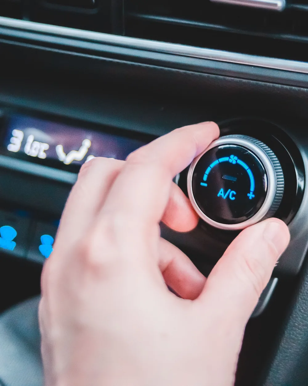 Hand adjusting climate controls inside a stationary vehicle