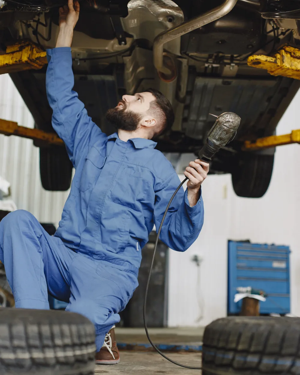 Mechanic inspecting components beneath a raised vehicle with a work light