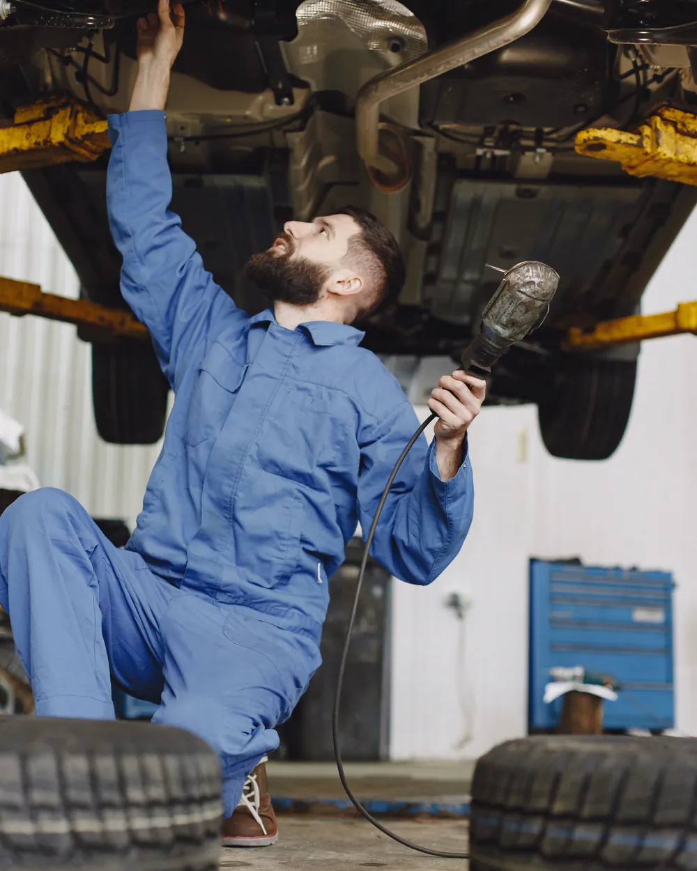 Mechanic in blue coveralls inspecting the underside of a raised vehicle