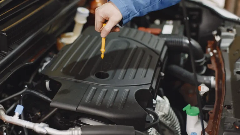 Technician checking engine oil with a dipstick in an open engine bay