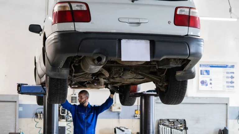 Technician inspecting the underside of a raised car in an automotive workshop