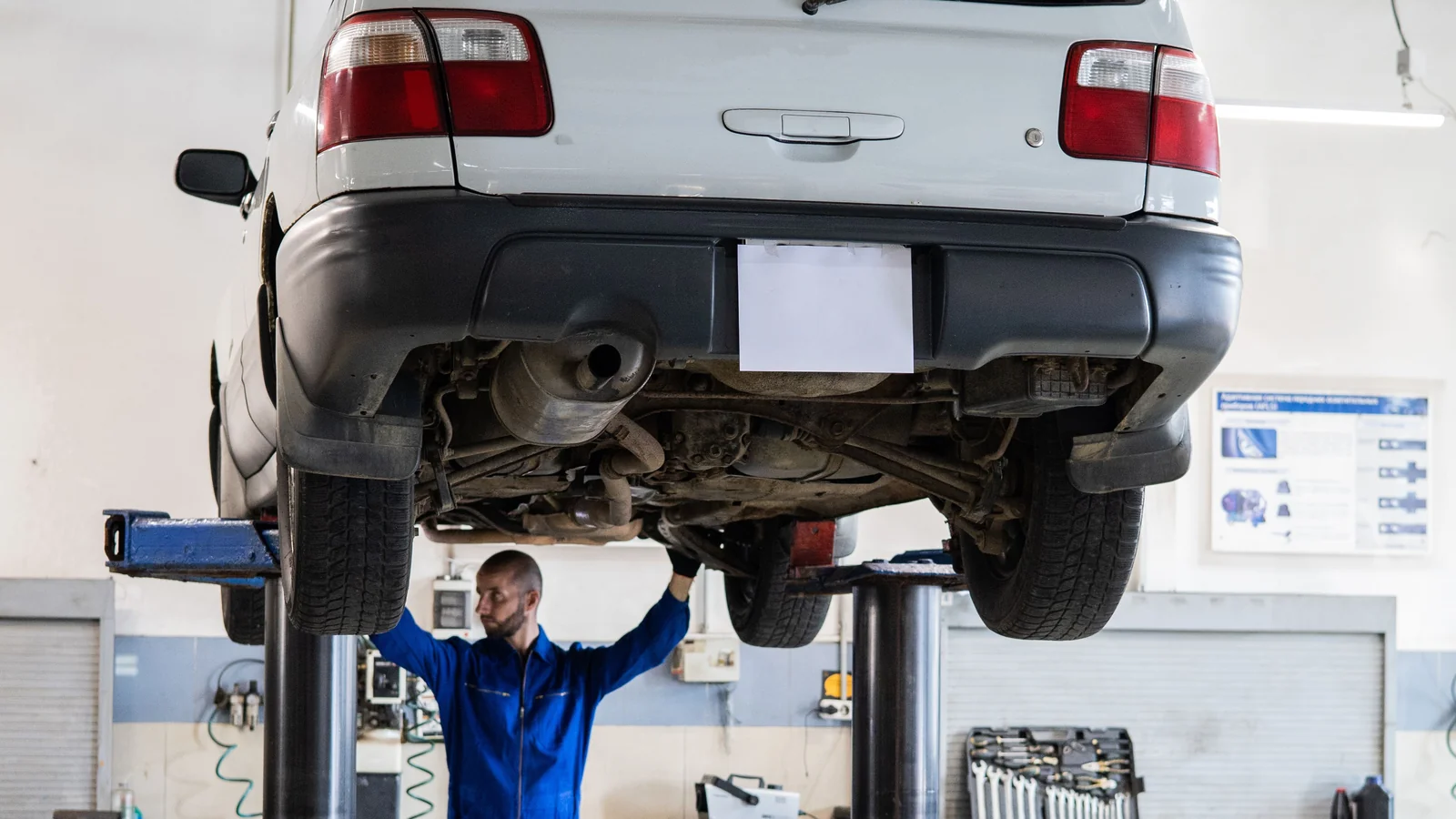 Technician inspecting the underside of a raised car in an automotive workshop
