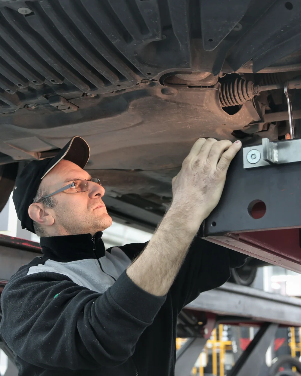  Technician inspecting the front underside of a car supported on a workshop lift