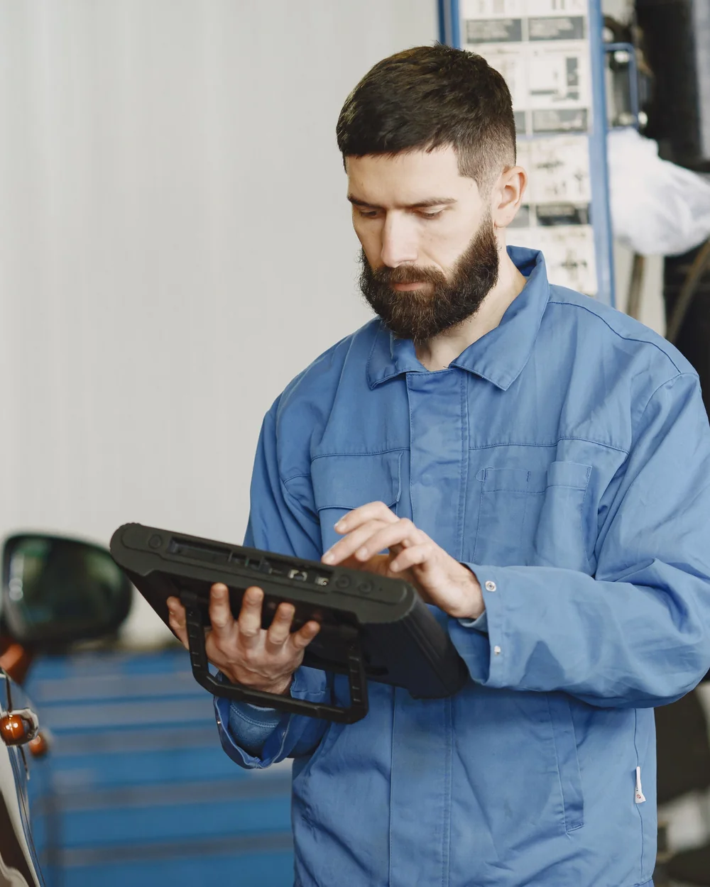 Technician using a diagnostic tablet beside a car in an automotive workshop