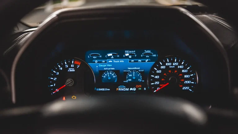 Yellow check engine light illuminated on a vehicle dashboard viewed through a steering wheel