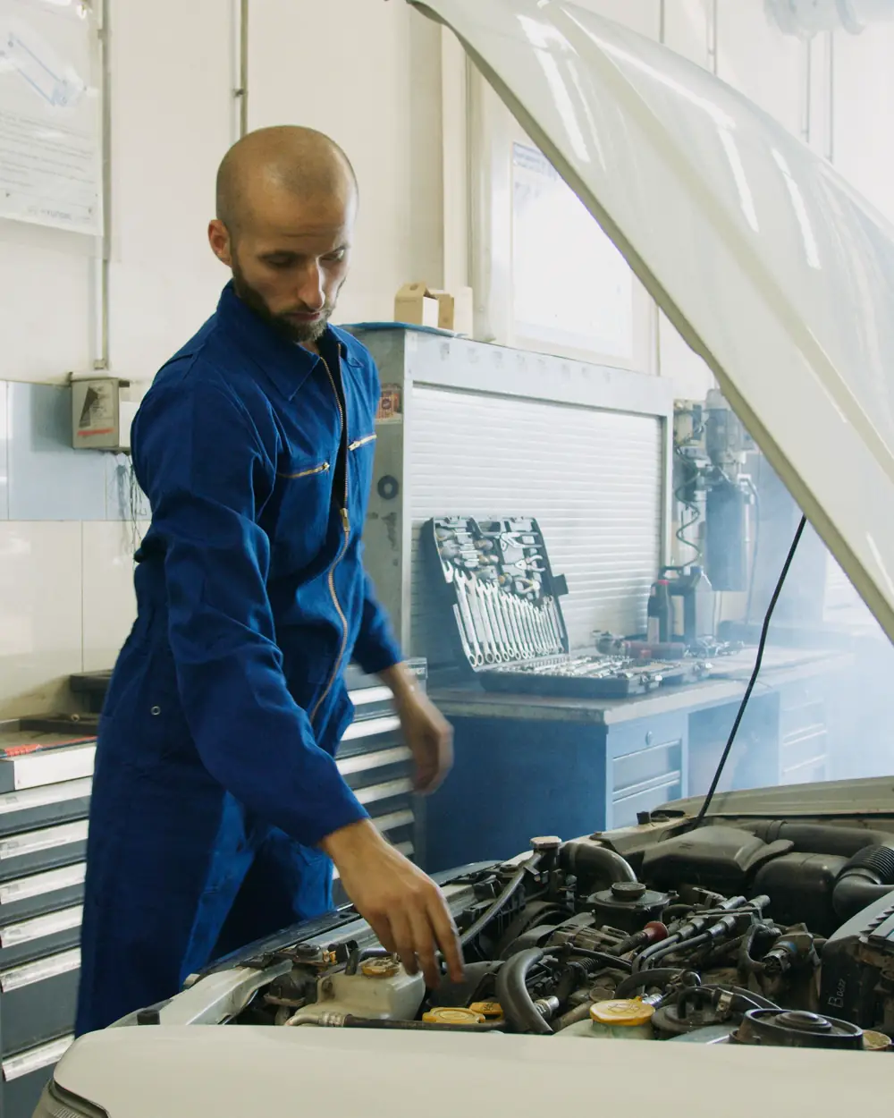 Technician inspecting an open vehicle engine bay in a workshop