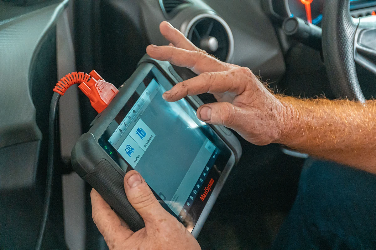 Technician holding a diagnostic scan tool beside a vehicle engine bay
